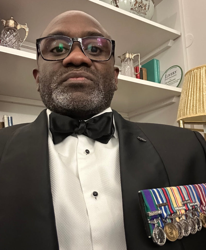 Man in a tuxedo with medals on a shelf in the background