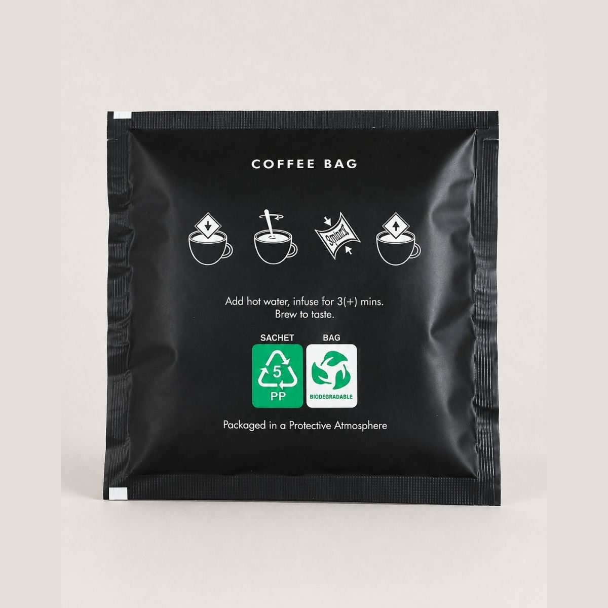 A single black coffee bag sachet with white printed text and icons, including coffee brewing steps and recycling symbols, photographed on a light neutral background.